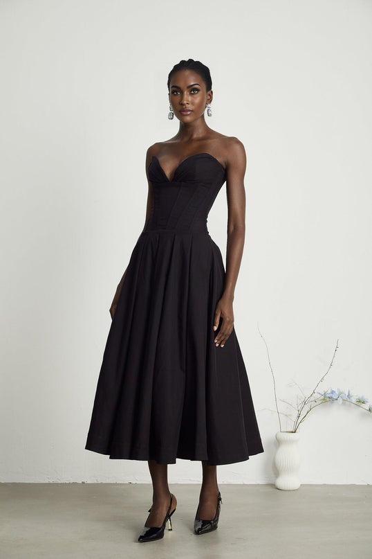 A black offshoulder midi dress with a corsetstyle bodice worn by a model standing against a plain background