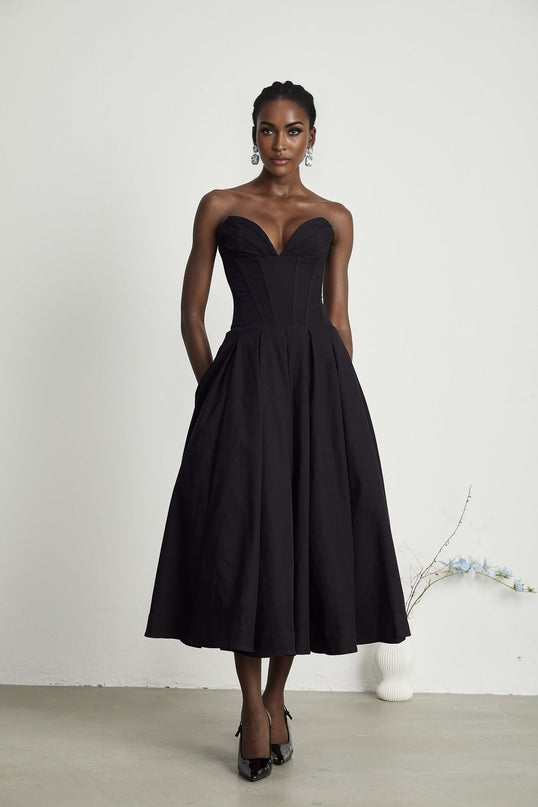A black offshoulder midi dress with a corsetstyle bodice worn by a model standing against a plain background