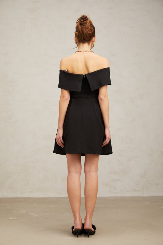 A black offshoulder mini dress with a belt featuring a fitted silhouette and short length named Greta