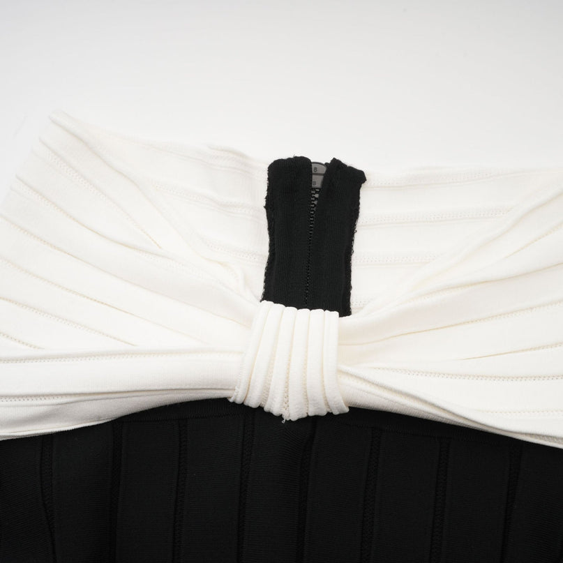 A black offshoulder mini dress with a bow detail and knit fabric worn by a model against a plain background