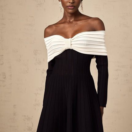 A black offshoulder mini dress with a bow detail and knit fabric worn by a model against a plain background