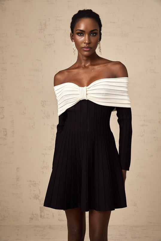 A black offshoulder mini dress with a bow detail and knit fabric worn by a model against a plain background