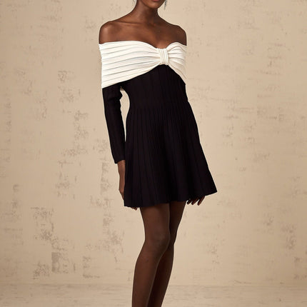 A black offshoulder mini dress with a knit texture and bow detail worn by a model named Justine
