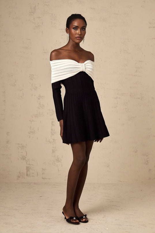 A black offshoulder mini dress with a knit texture and bow detail worn by a model named Justine