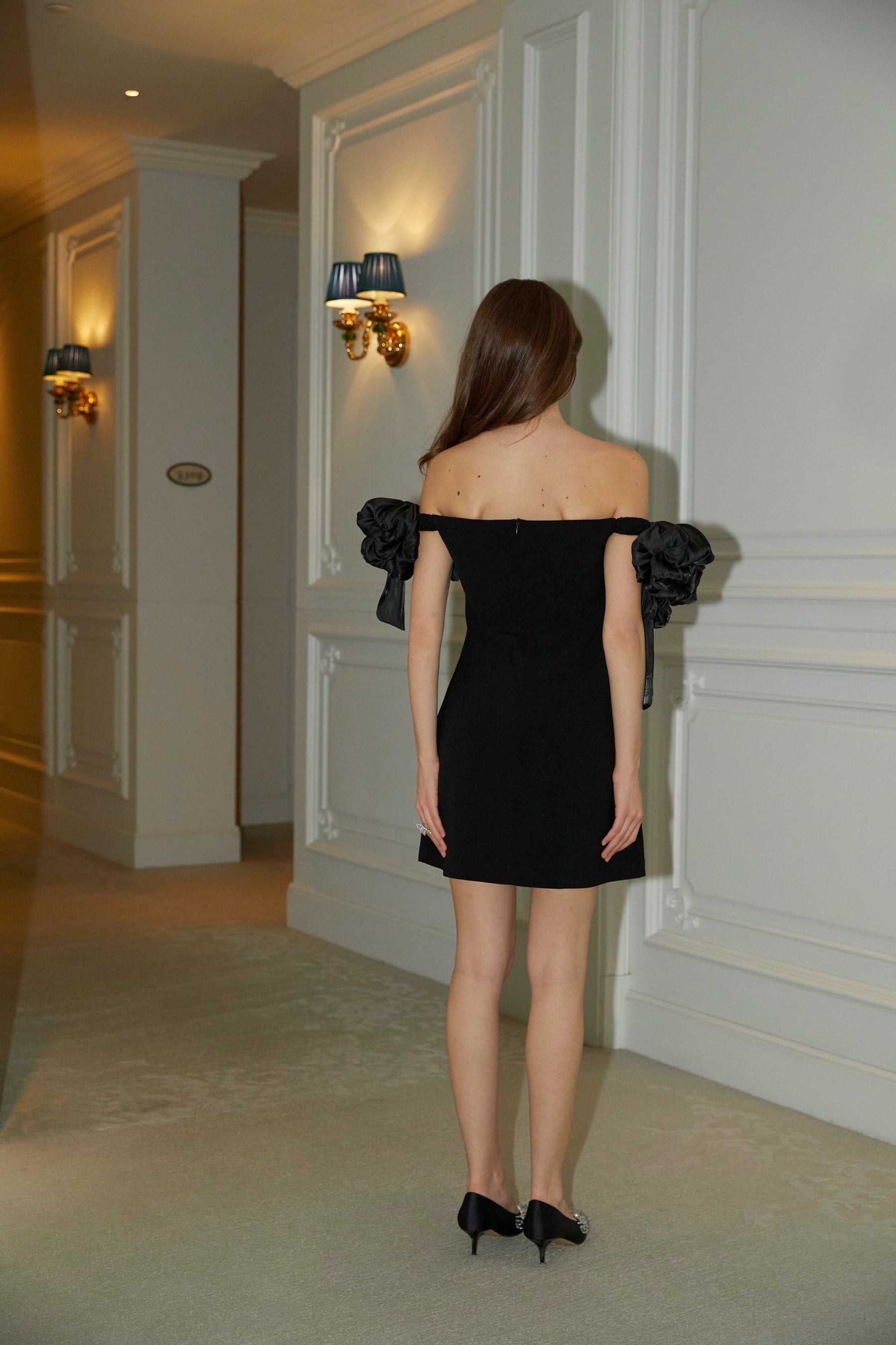 A black offshoulder mini dress with floral details named Erica worn by a model against a plain background