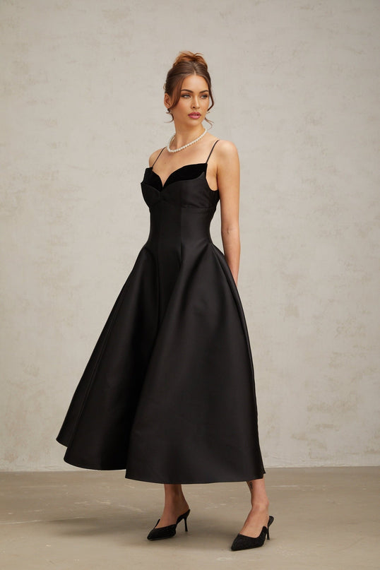 A black pleated midi dress with a flared silhouette worn by a model standing against a plain background