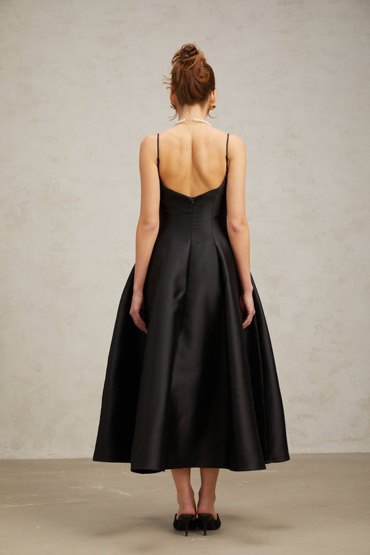 A black pleated midi dress with a flared skirt named Roxane hanging on a display