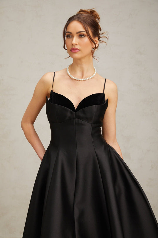 A black pleated midi dress with a flared skirt worn by a model standing against a plain background