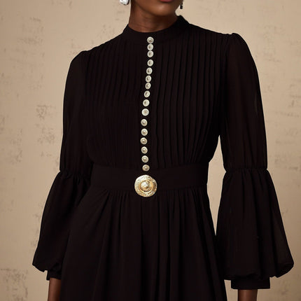 A black pleated midi dress with button front closure and long sleeves on a white background