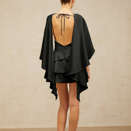 A black satin mini dress with ruffled details and a shawl panel accent worn by a model against a plain background