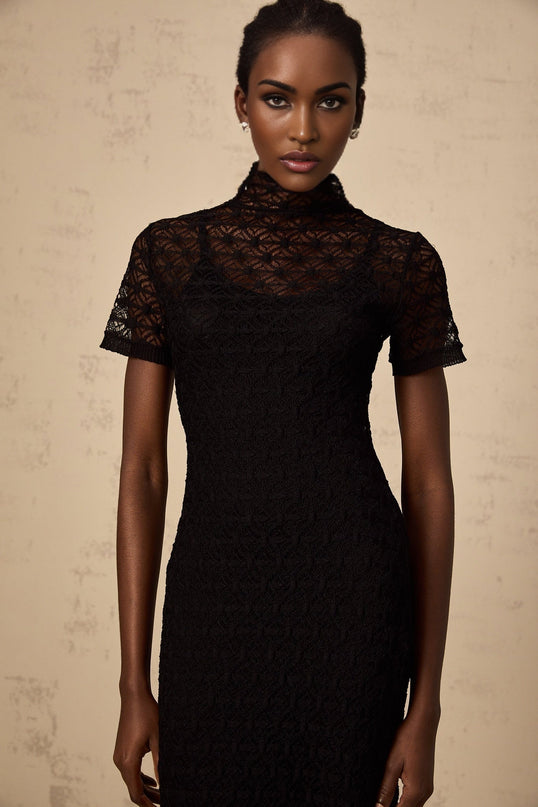 A black semi sheer knit midi dress on a model standing against a plain background