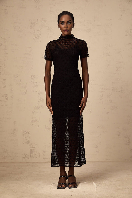 A black semi sheer knit midi dress worn by a model standing against a plain background