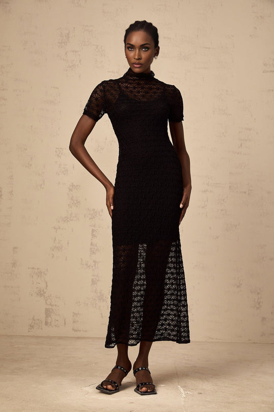 A black semi sheer knit midi dress worn by a model standing against a plain background