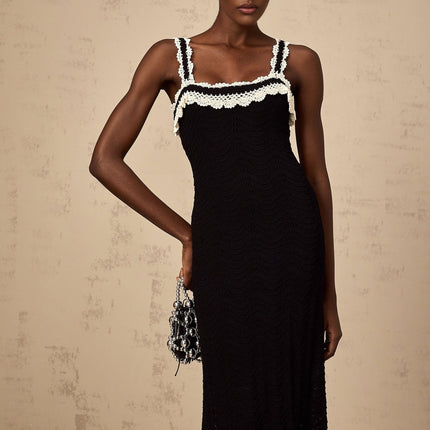 A black sleeveless midi dress with a crochet knit pattern worn by a model standing against a plain background