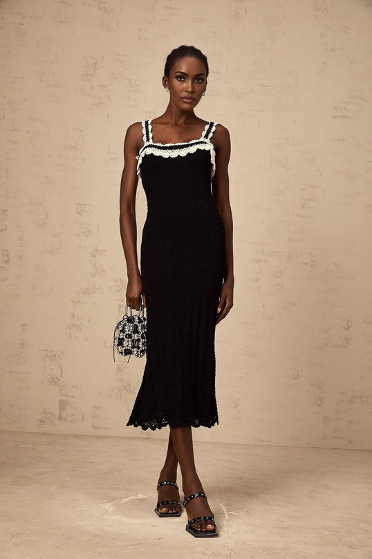 A black sleeveless midi dress with intricate crochet knit detailing throughout the garment