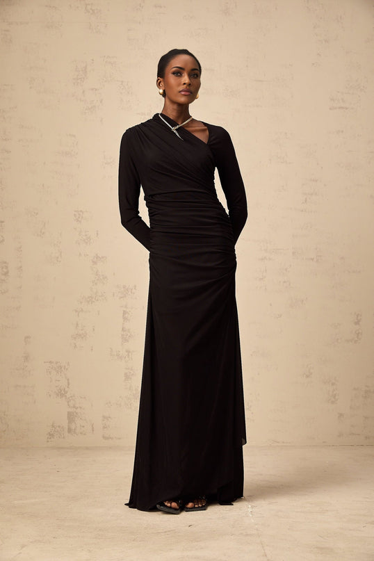 A black tulle maxi dress with asymmetric cutout details and an uneven hemline worn by a model against a plain background