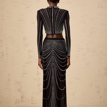 A black twopiece outfit consisting of a mesh top and skirt adorned with rhinestones The top has long sleeves and the skirt is knee length Both pieces feature a sparkly rhinestone pattern throughout the sheer mesh fabric
