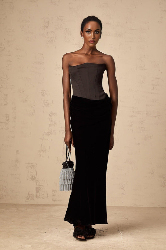 A black velvet maxi dress with an offshoulder neckline and long skirt worn by a model against a plain background