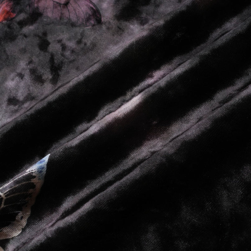 A black velvet midi dress with a butterfly print pattern worn by a model standing against a plain background