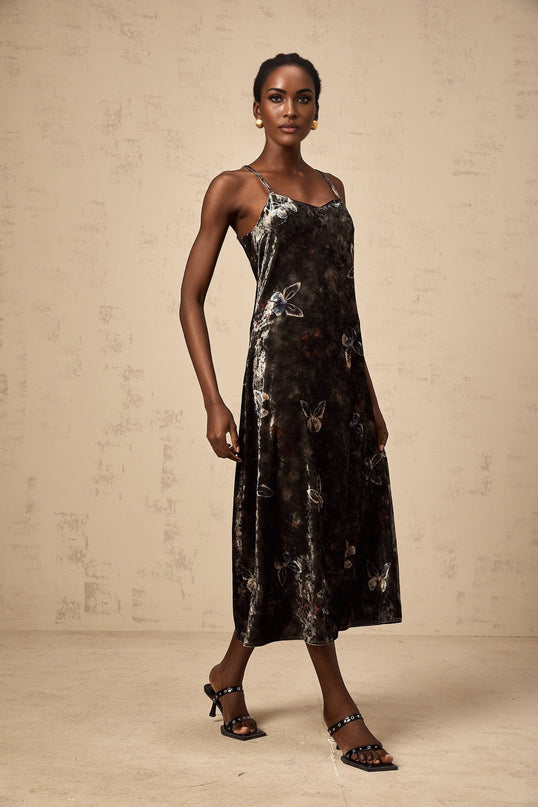 A black velvet midi dress with a butterfly print pattern worn by a model standing against a plain background