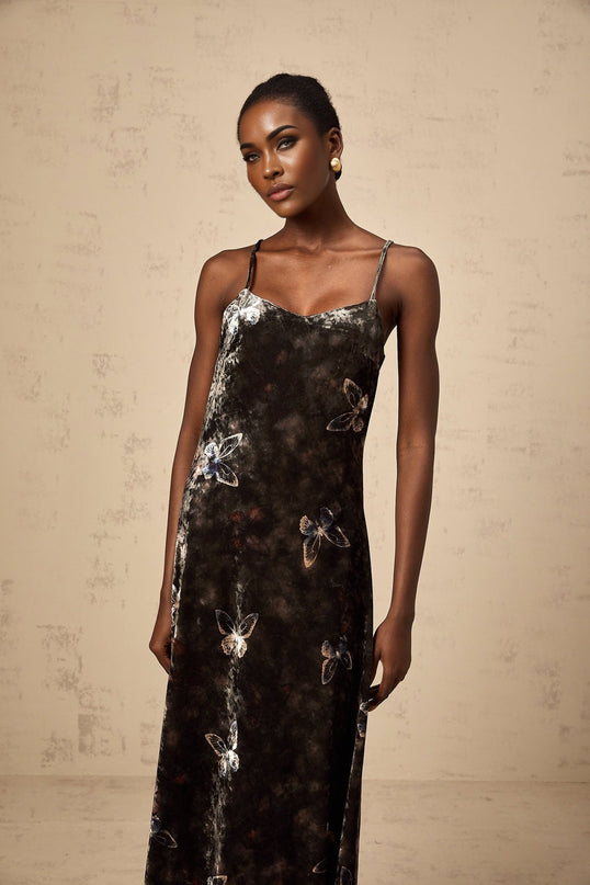 A black velvet midi dress with white butterfly prints covering the fabric The dress features long sleeves and a flowing silhouette reaching below the knees