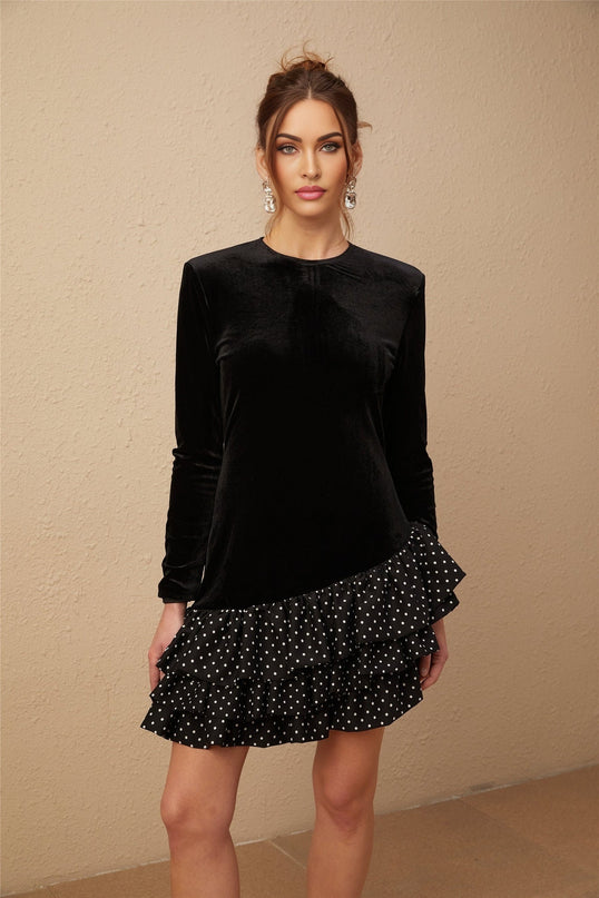 A black velvet mini dress with white polka dots featuring ruffled panels and a flared skirt