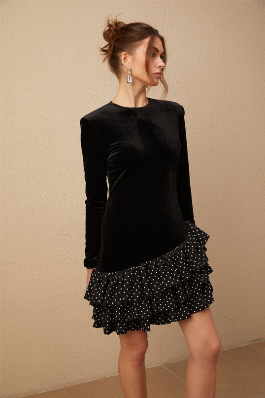 A black velvet mini dress with white polka dots featuring ruffled panels and a short hemline