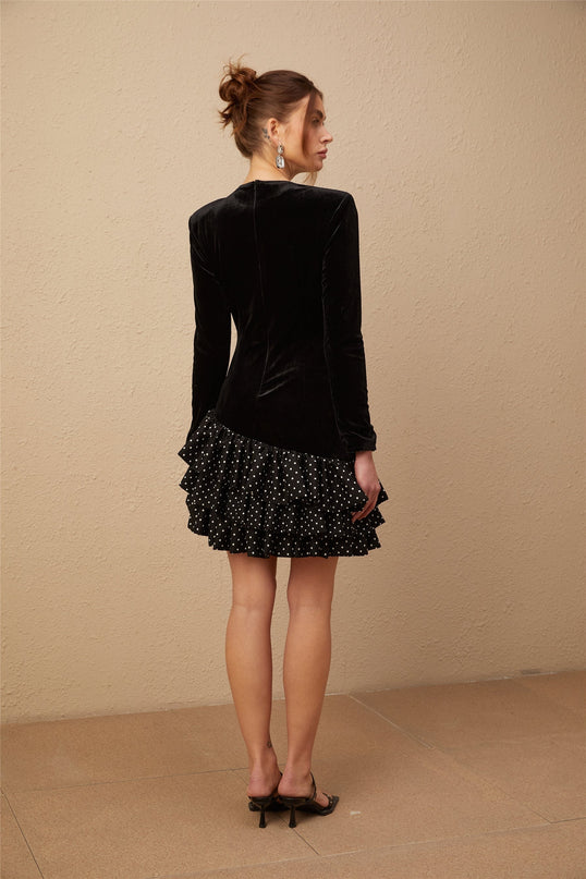 A black velvet mini dress with white polka dots featuring ruffled panels and a short hemline