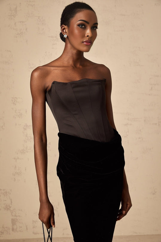 A black velvet off shoulder maxi dress with a long flowing skirt worn by a model against a plain background