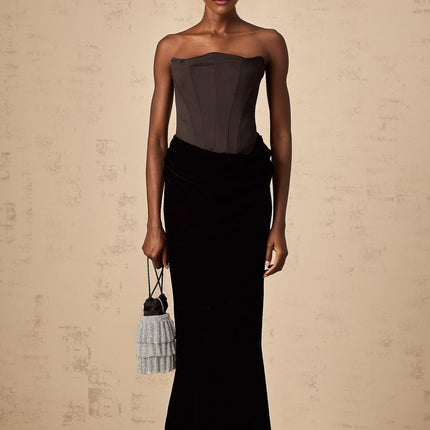 A black velvet offshoulder maxi dress with a long flowing skirt worn by a model standing against a plain background
