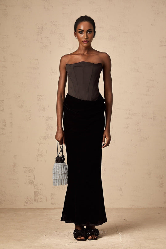 A black velvet offshoulder maxi dress with a long flowing skirt worn by a model standing against a plain background