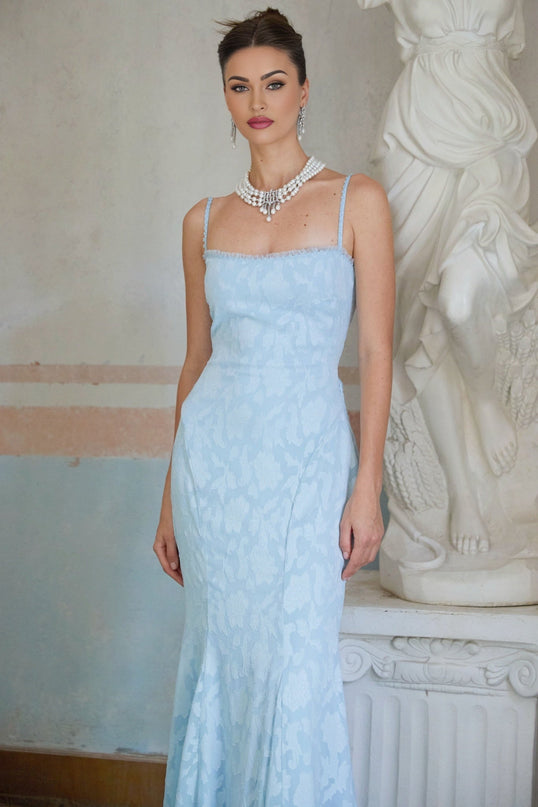 A blue flared maxi dress with laceup detail and jacquard pattern on a model against a plain background