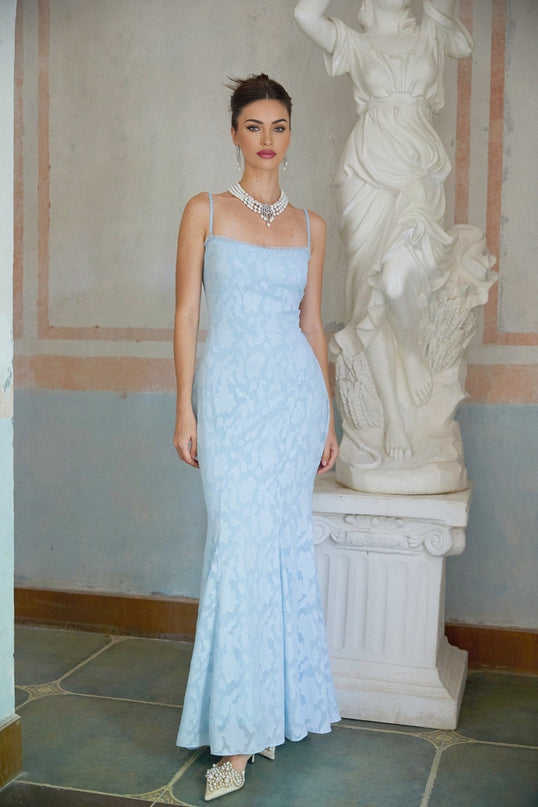A blue flared maxi dress with laceup detail and jacquard pattern worn by a model standing in a neutral setting
