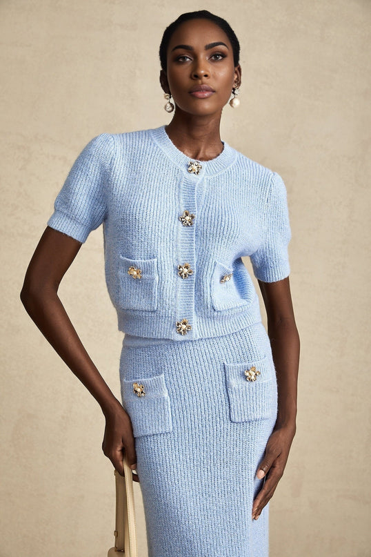 A blue knit matching set featuring a blouse and skirt The top is a long sleeve knit blouse paired with a coordinating knee length skirt Both pieces are in a soft blue color creating a cohesive and stylish outfit