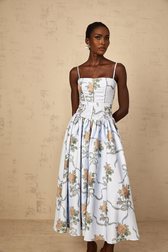 A blue midi dress with a floral print pattern worn by a woman standing in a relaxed pose