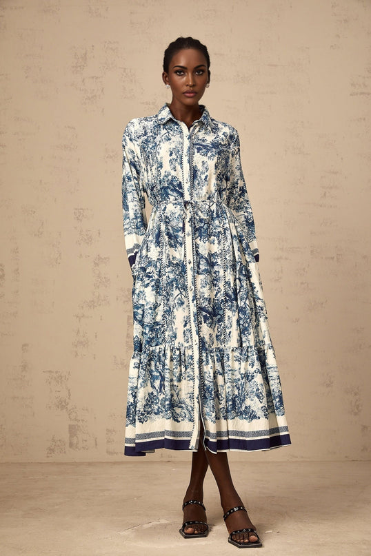 A blue midi dress with a graphic print pattern featuring the Adélaïde design worn by a female model against a plain background