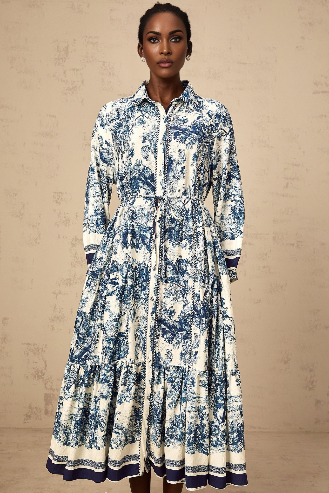A blue midi dress with a graphic print pattern named Adelaide worn by a model standing against a plain background