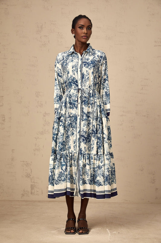 A blue midi dress with a graphic print pattern named Adelaide worn by a model standing against a plain background