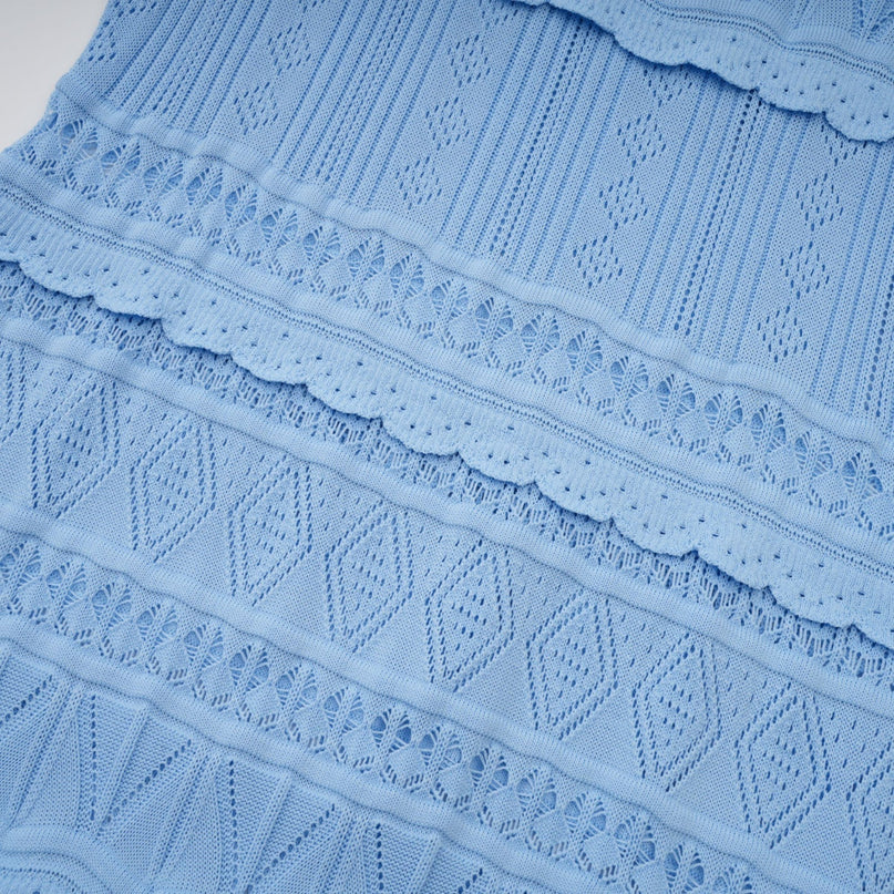 A blue midi dress with crochet knit pattern and ruffled trim details worn by a model standing in a neutral setting