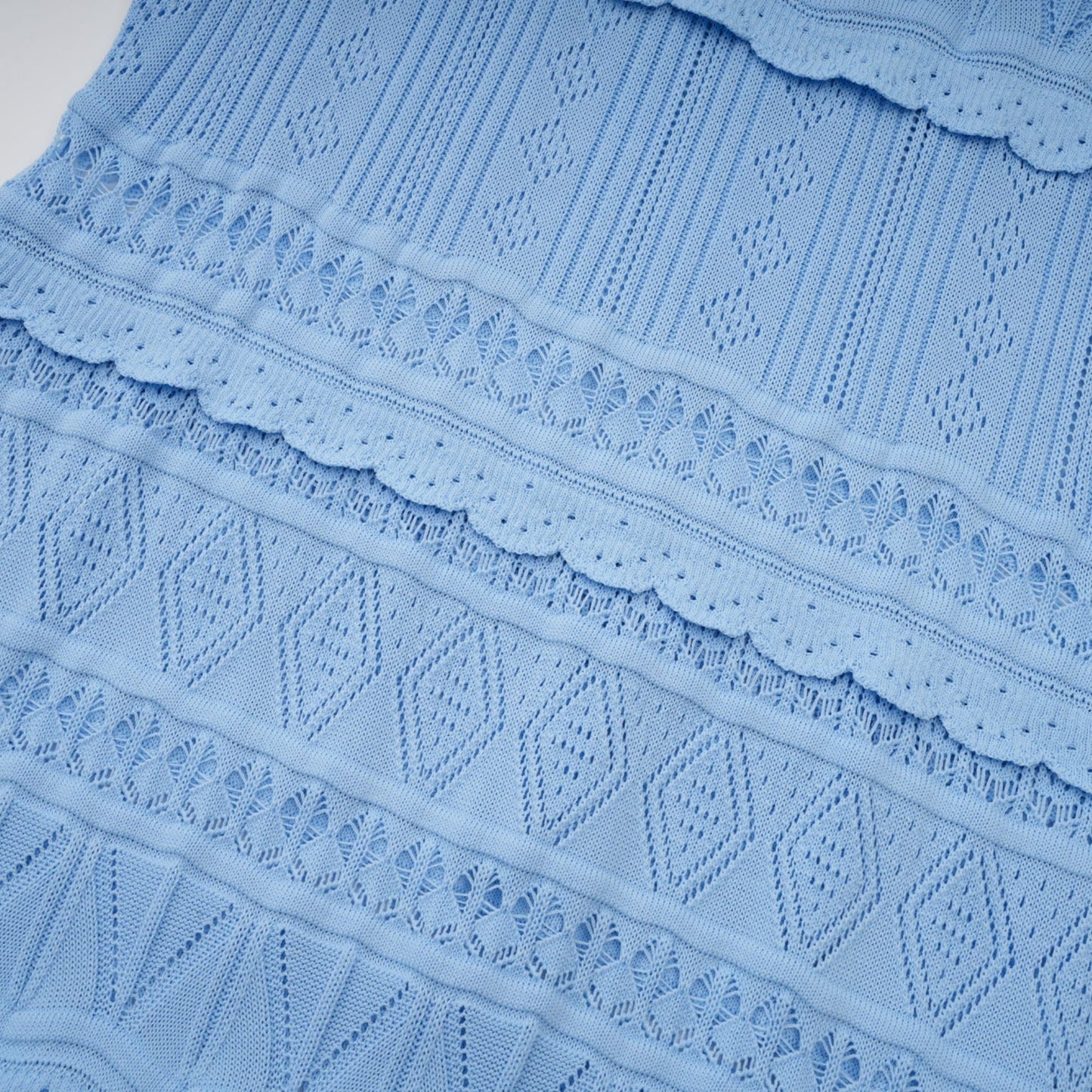 A blue midi dress with crochet knit pattern and ruffled trim details worn by a model standing in a neutral setting