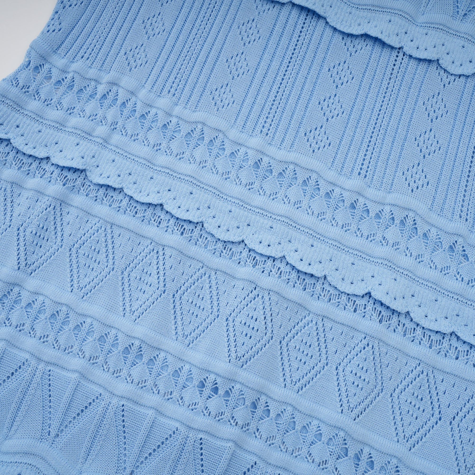 A blue midi dress with crochet knit pattern and ruffled trim details worn by a model standing in a neutral setting