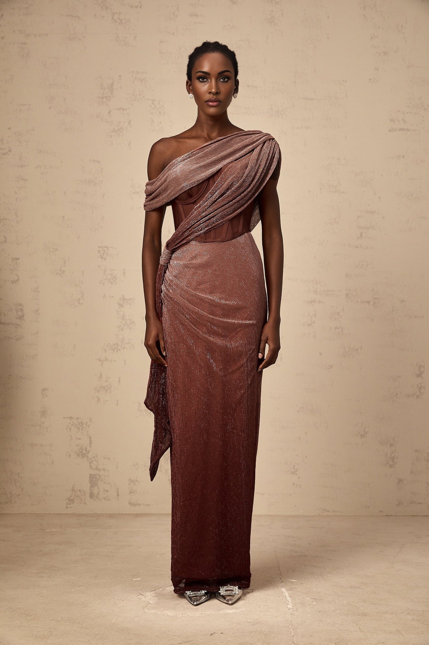 A brown maxi dress with a corsetstyle top featuring ribbon design details and a long flowing skirt