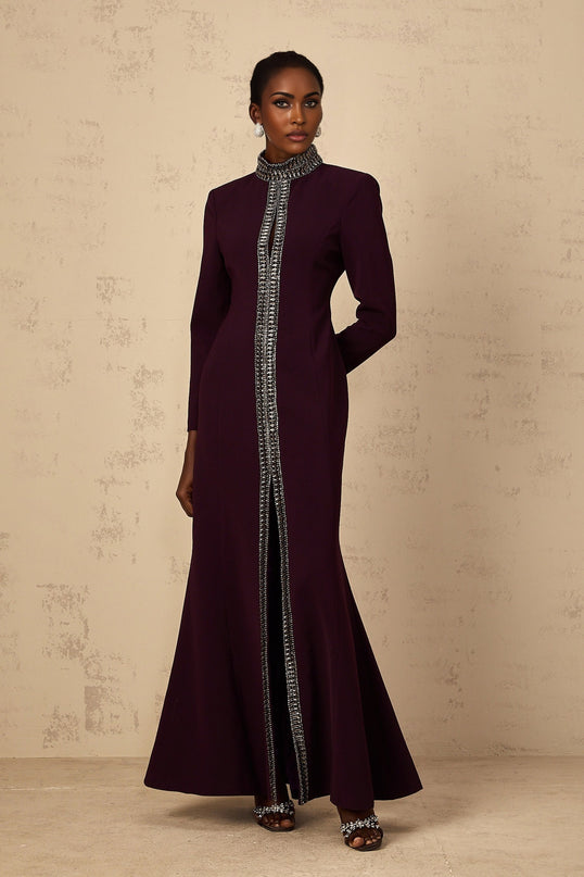 A burgundy flared maxi dress with embellishments worn by a model standing against a plain background