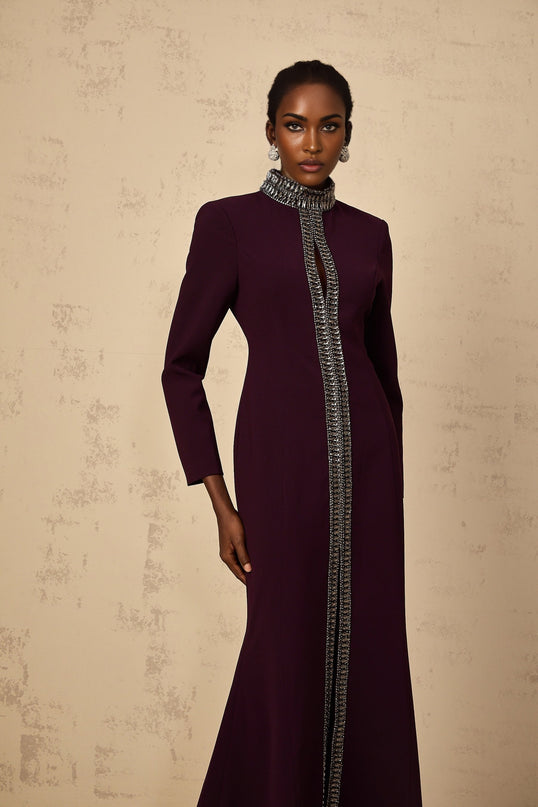 A burgundy floorlength maxi dress with a flared silhouette and embellished details worn by a model against a plain background