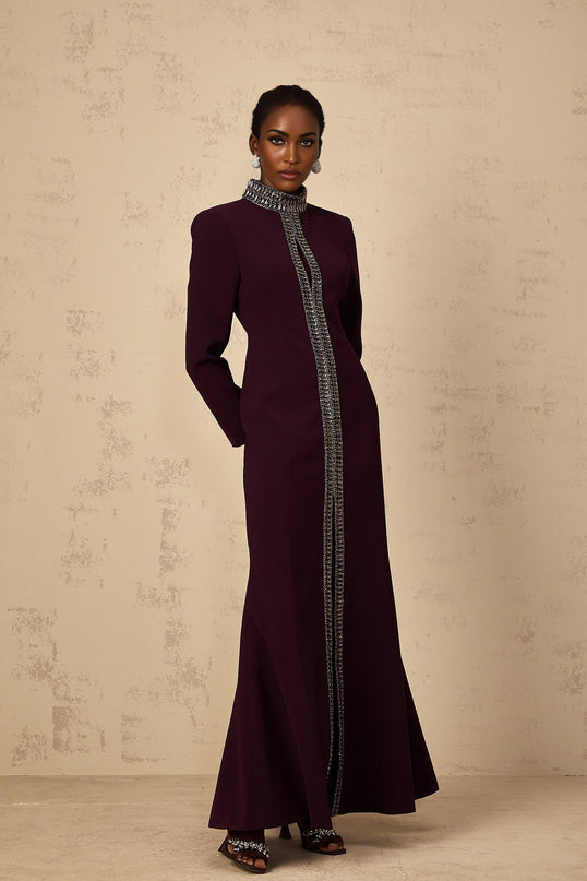 A burgundy floorlength maxi dress with a flared skirt and embellished details worn by a model against a plain background