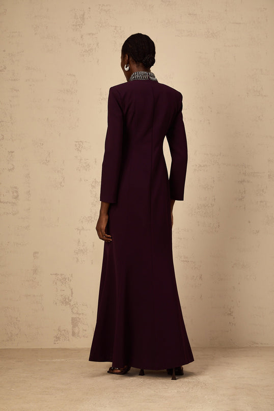 A burgundy maxi dress with flared skirt and embellished details worn by a model standing against a plain background