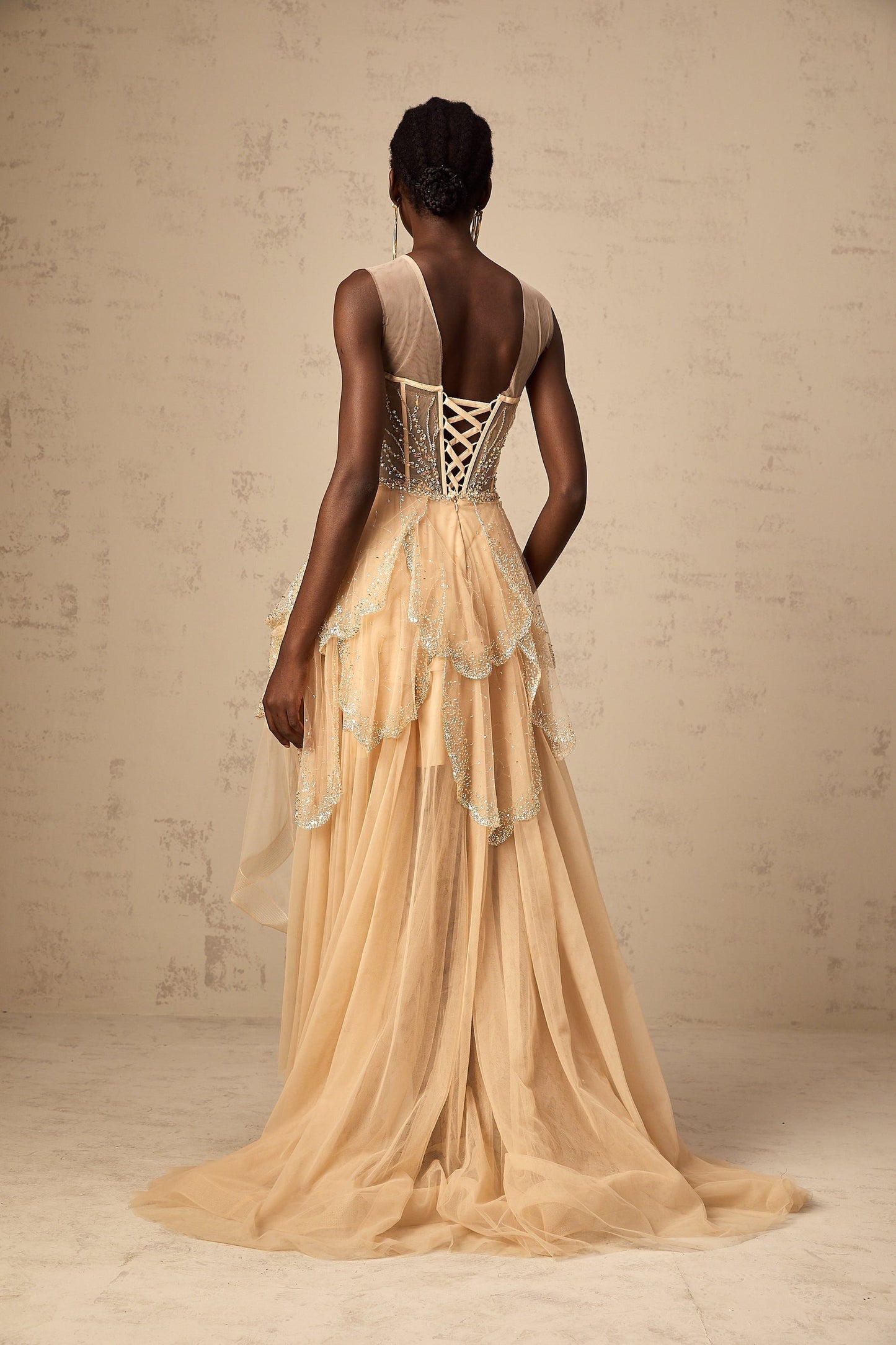 A champagnecolored formal gown with a highlow hemline featuring daisyinspired embellishments and a flowing silhouette