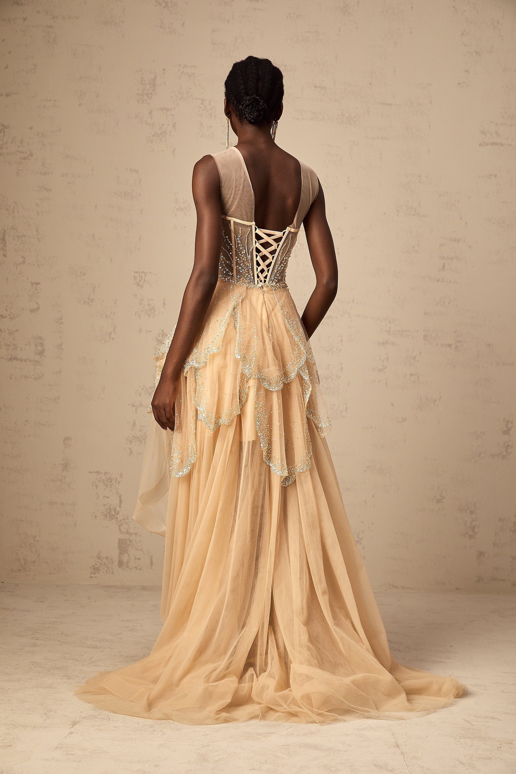 A champagnecolored formal gown with a highlow hemline featuring daisyinspired embellishments and a flowing silhouette