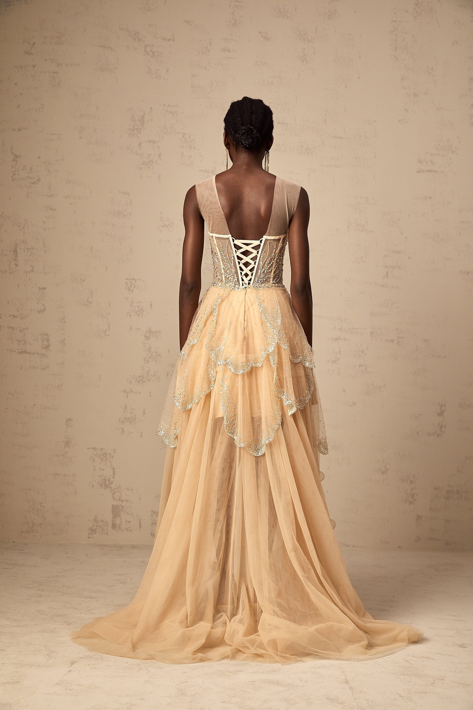 A champagnecolored formal gown with a highlow hemline featuring daisyshaped embellishments and a flowing silhouette