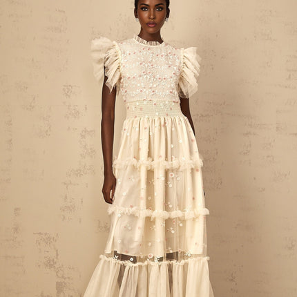A cream white maxi dress with floral embroidery and tiered tulle skirt worn by a woman